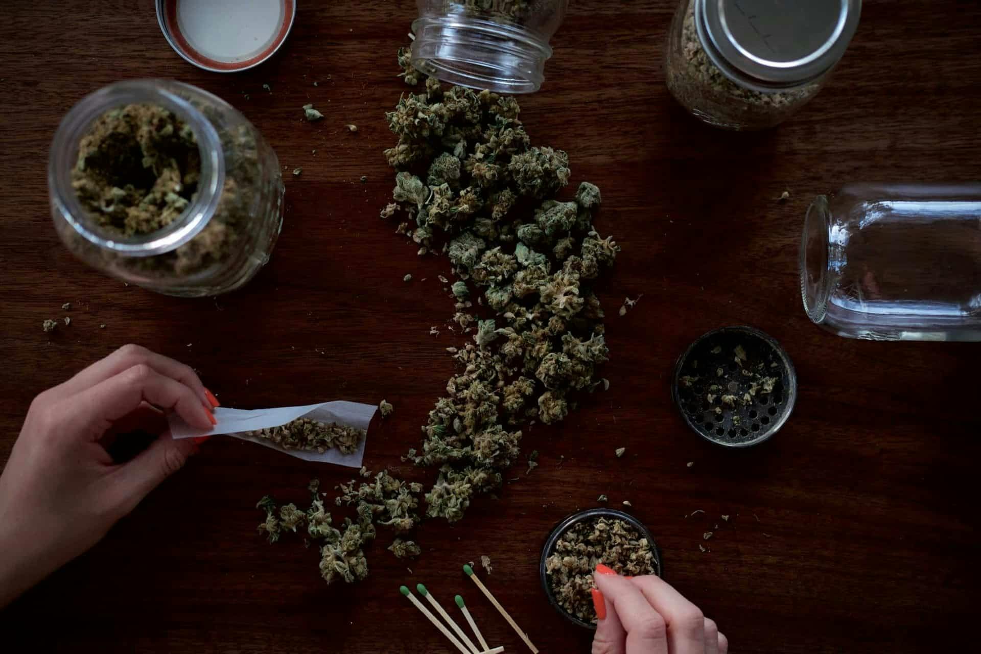 Photo of someone rolling a joint with mason jars filled with weed.