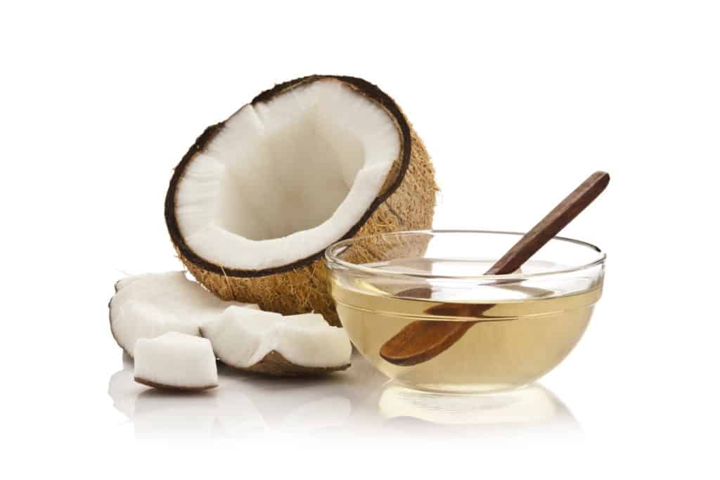 Half opened coconut with a glass bowl of oil