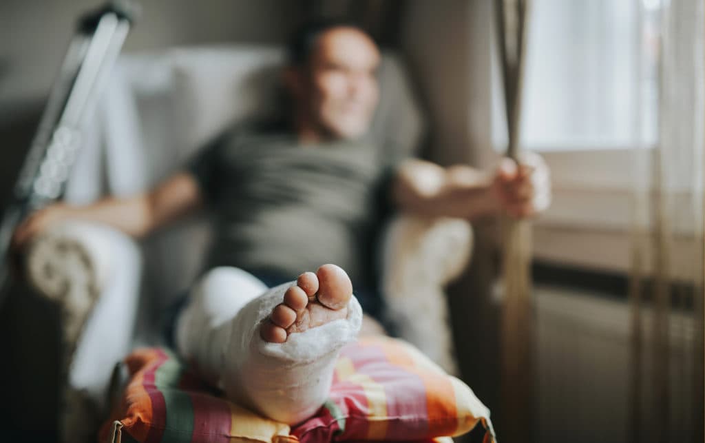 man lays with his injured leg in cast propped up