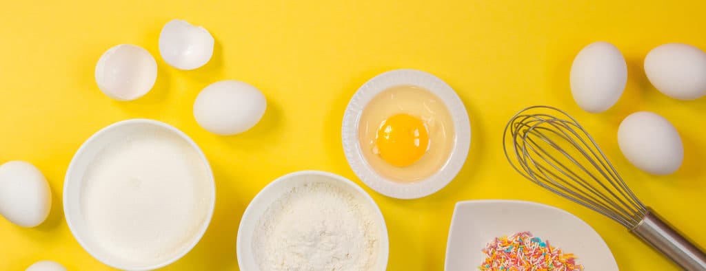 Eggs, flour, sugar and ingredients for baking on a yellow backgr