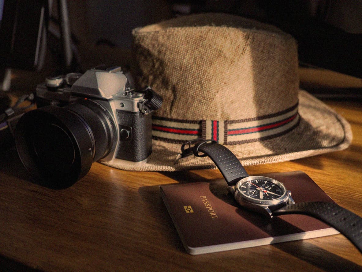 Closeup view of the passport, wrist watch, camera and a hat on the wooden desk.