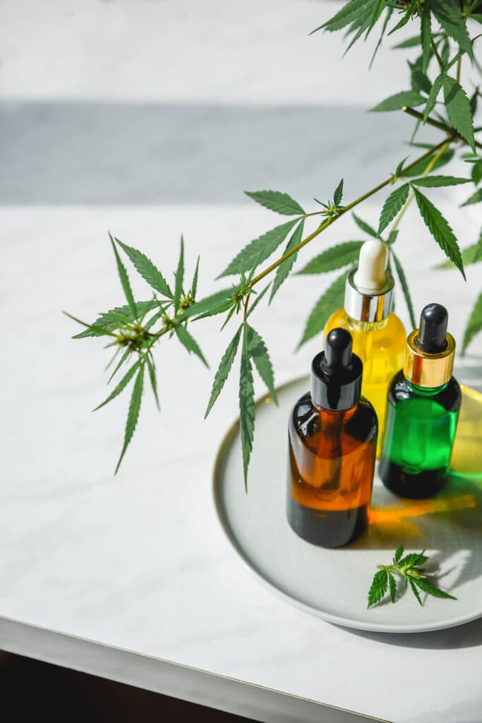 Different glass bottles with CBD OIL, THC tincture and cannabis leaves on yellow background. Flat lay, minimalism. Cosmetics CBD oil.