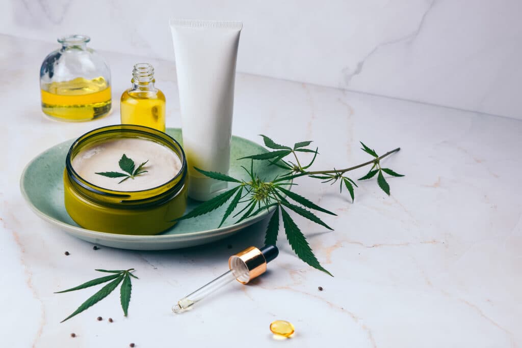 Cosmetics with cannabis oil on a turquoise plate on a light marble background. Concept of luxury skin care.