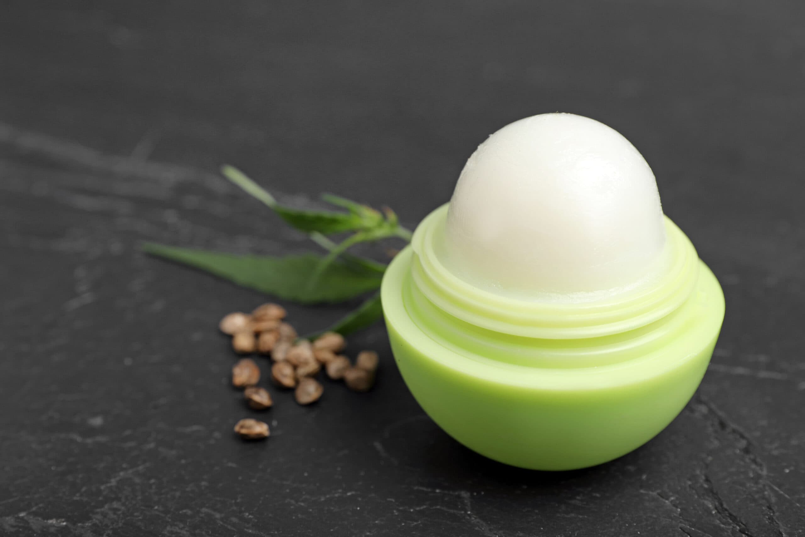 CBD Lip balm, hemp leaf and seeds on black table, closeup. Natural cosmetics