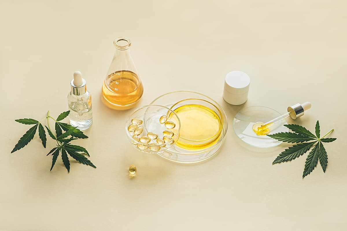 Products with CBD oil in laboratory glassware, Petri dishes, Capsules, cosmetics, THC tincture, pipette, with CBD oil and hemp leaves, light background. The concept of medical cannabidiol