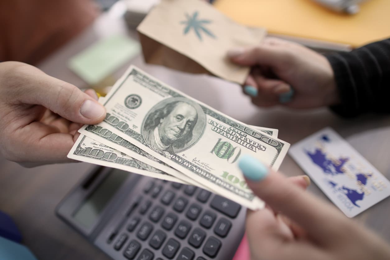 Close-up of persons hands giving money and taking package with ganja marihuana sign on it. Pack with cannabis sign on table. Sale of medical marijuana concept