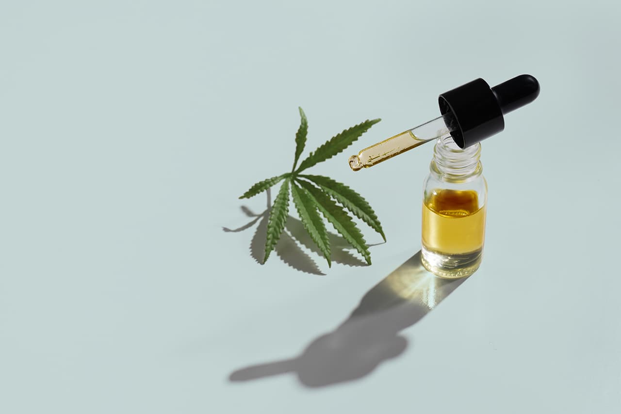 Set of marijuana features with CBD oil product on glass bottle with dropper lid, hemp leaf and dry bud, hemp leaf and bud arranged on empty background. Cannabis product concept.