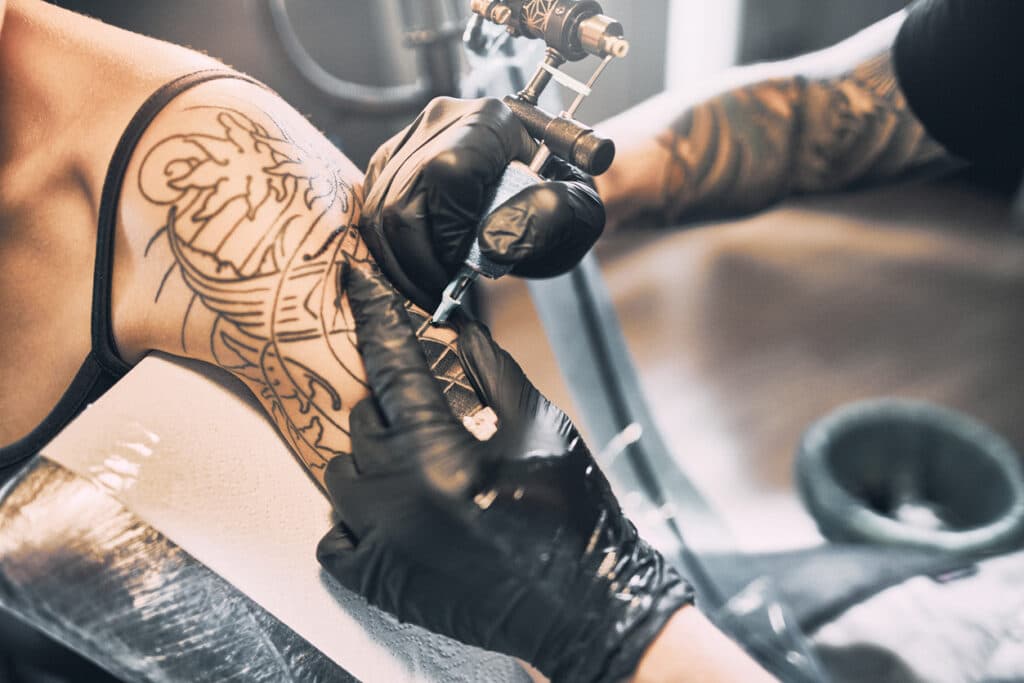 Artist Tattooing woman’s shoulder in tattoo studio