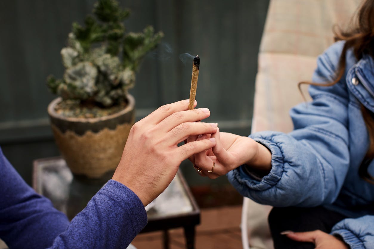 Closeup of a two young friends passing a joint to each other while sitting outside on their patio