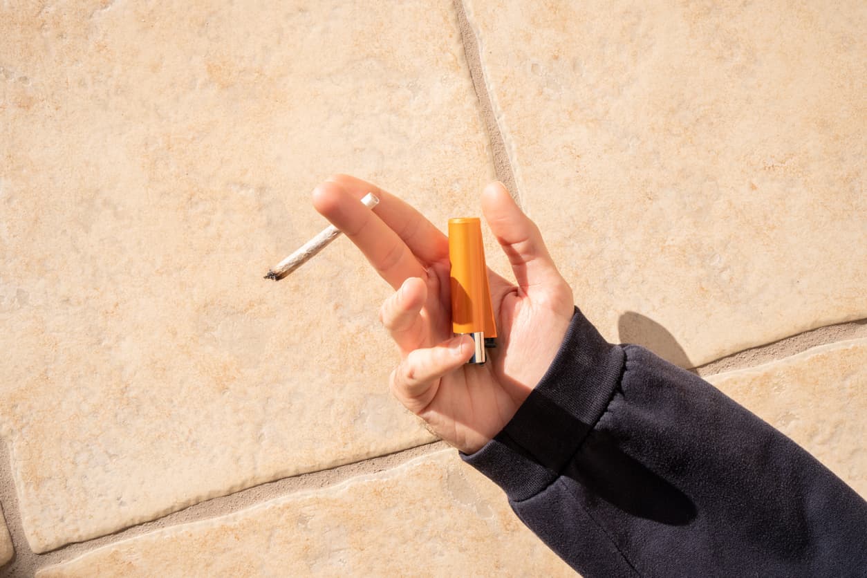 Unrecognized person lying on the floor holding a marijuana joint on sunny day. Concept of relaxing while smoking marijuana