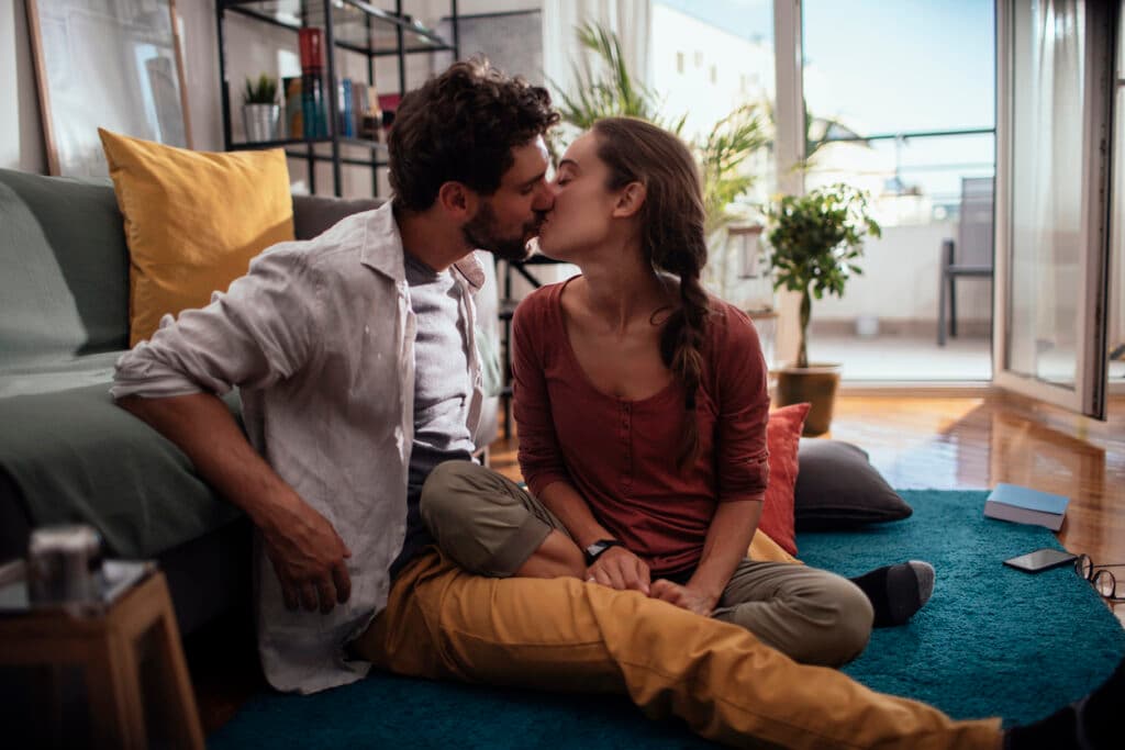 Young couple kissing while sitting on their living room floor