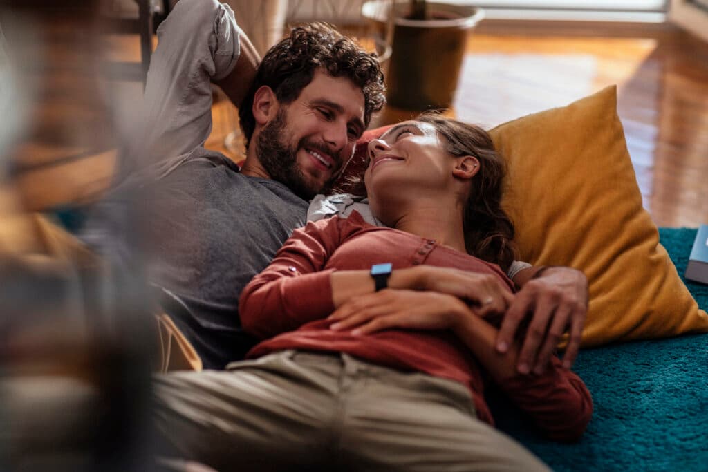 Young couple cuddling while lying down on their living room floor