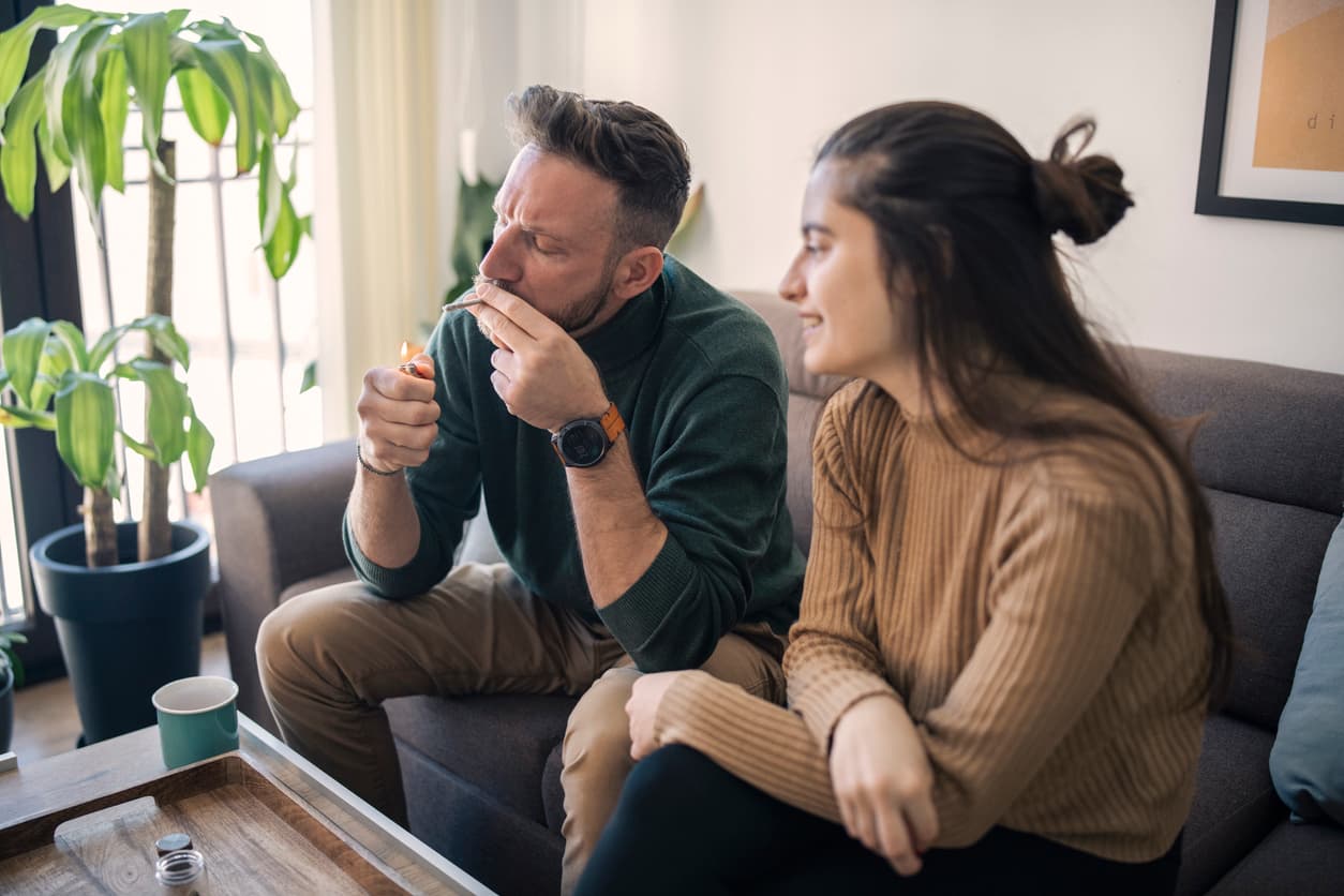 Man and woman smoking marijuana joint together at home.