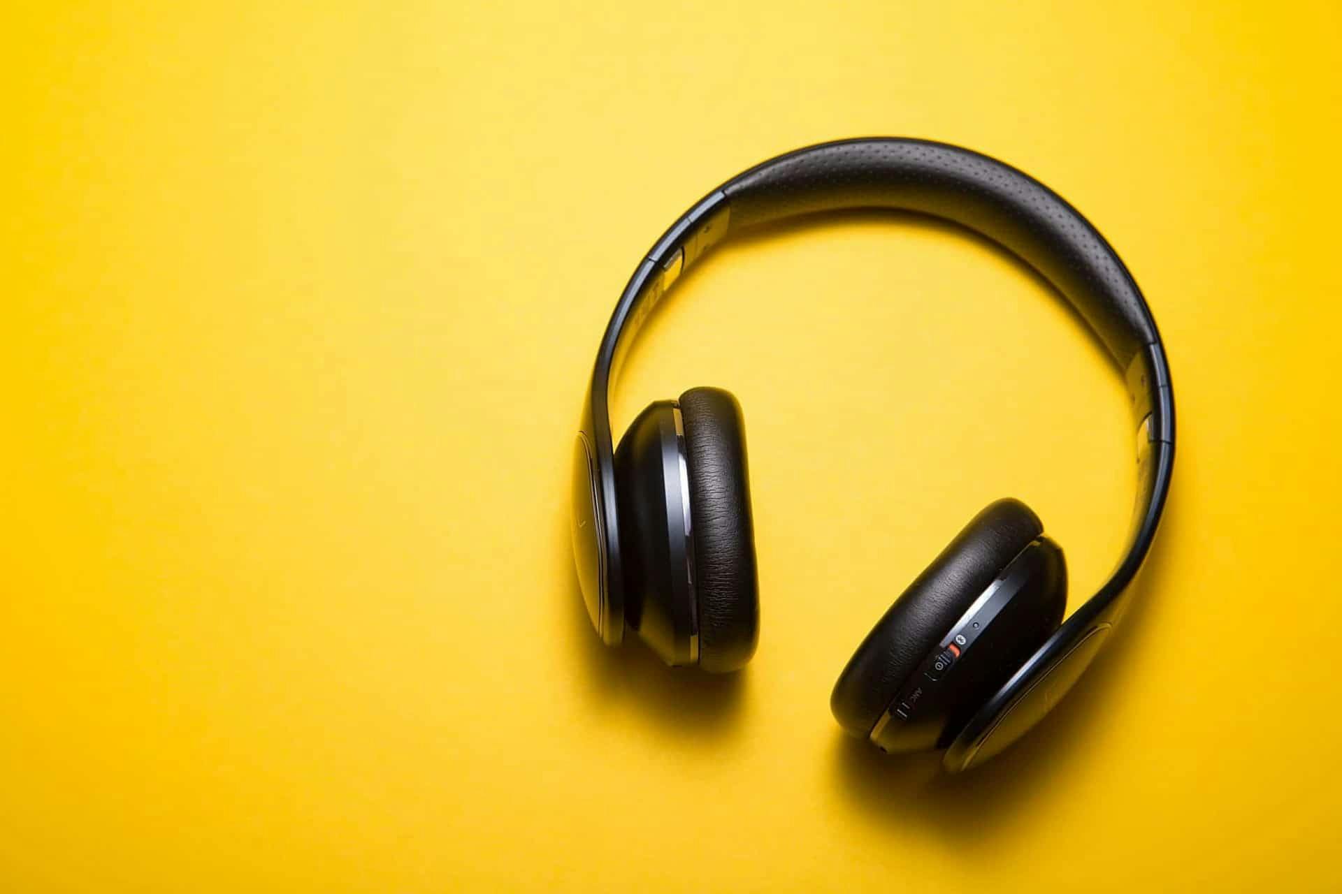 Photo of black headphones in front of a yellow backdrop.