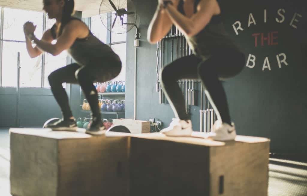 Photo of two women doing box jumps at a gym.