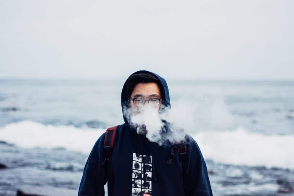 Man blowing a cloud of smoke in front of the ocean