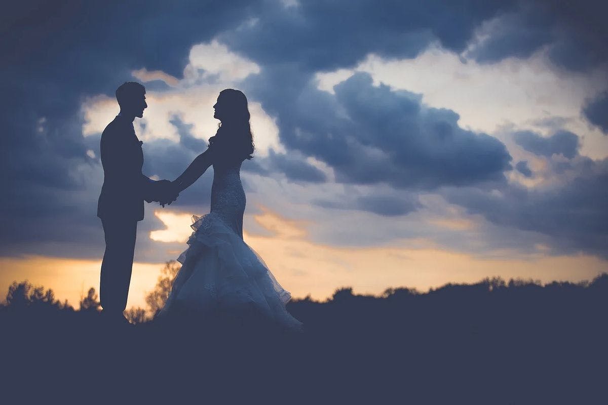 A married couple holds hands in front of the sunset after their wedding, by Pexels via Pixabay