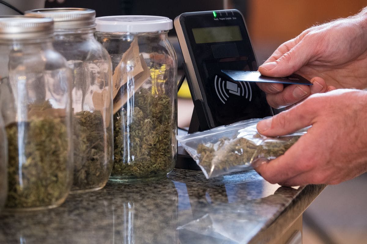 A man purchases cannabis from a budtender at a local dispensary, by nattrass via iStock