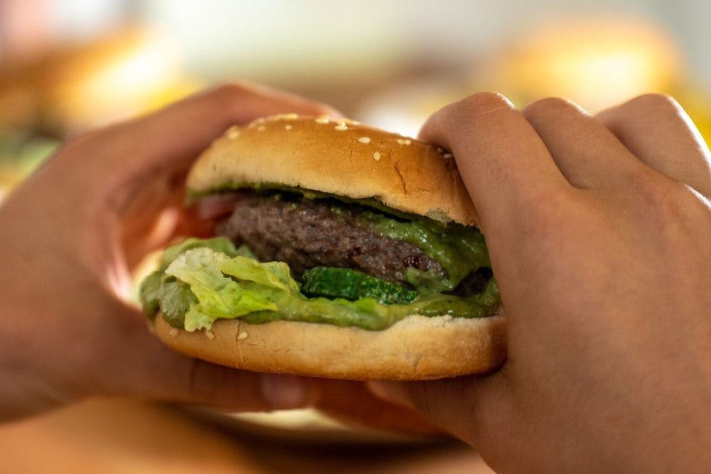 A pair of hands reach out to grab a hamburger, by Mammiya via Pixabay