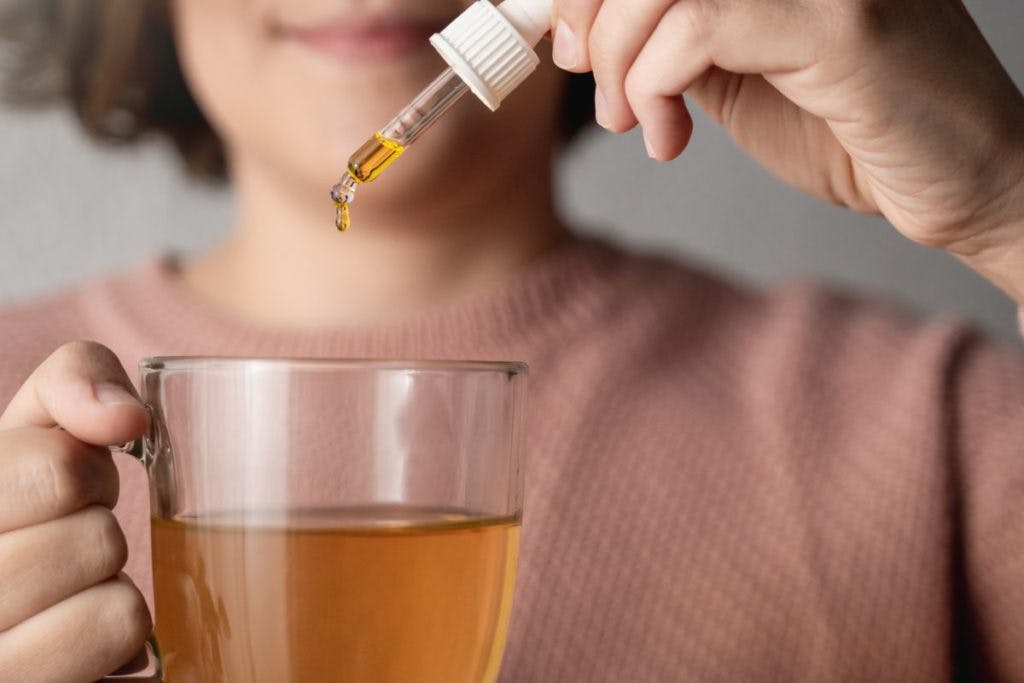 A woman adds hemp-based CBD oil to a cup of tea, by Vanessa Nunes via iStock