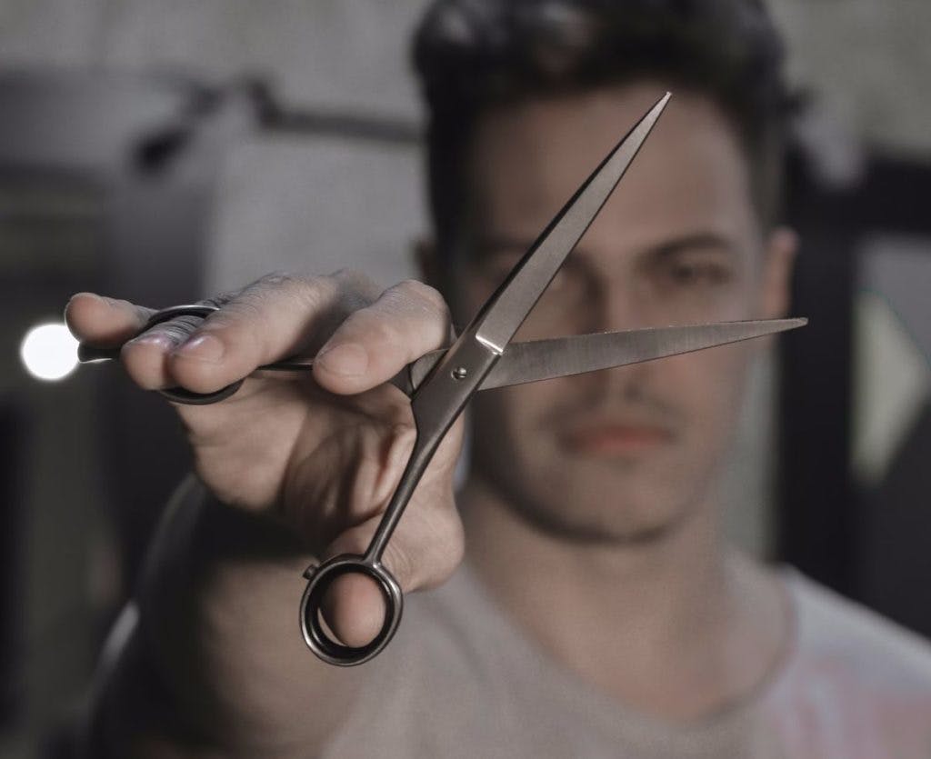 A man holding a pair of scissors, b Ta Focando via Unsplash