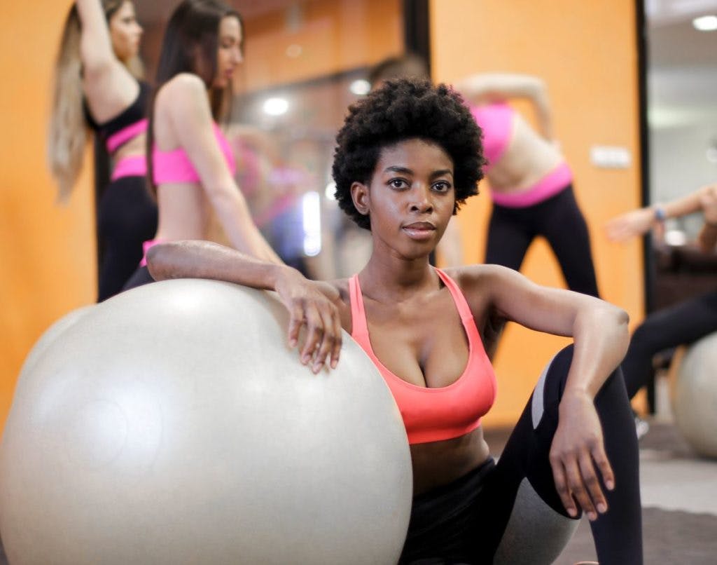 A woman crouches next to an exercise ball, by Andrea Piacquadio via Pexels