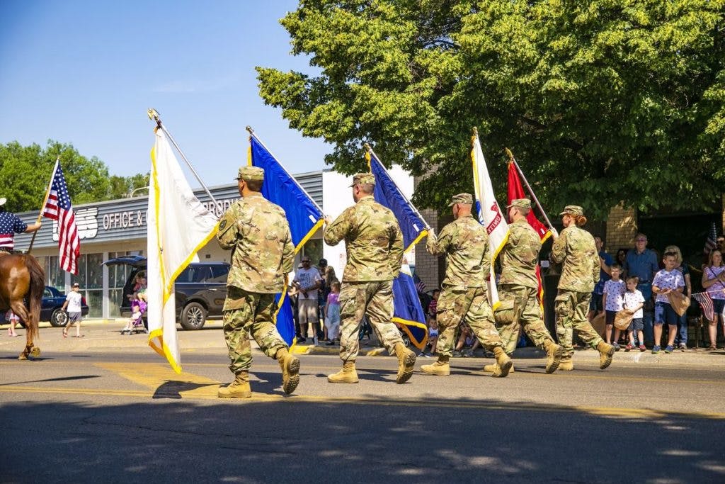 American military vets carrying flags in a street parade, by Ian MacDonald via Unsplash