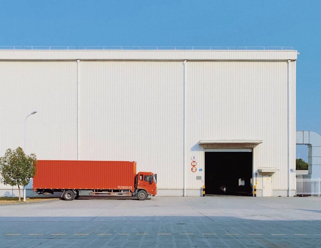 A red shipping truck in front of a white building, by Han Chenxu via Unsplash