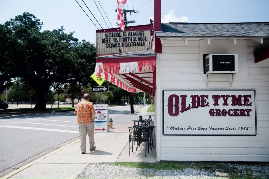 A man stands outside the Olde Tyme Grocery in Layfayette, Louisana, by Victor Martin via Unsplash