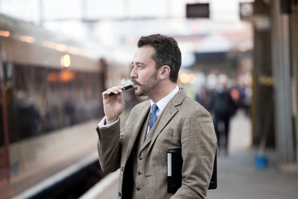 A man wearing a suit uses a vaporizer near the train, by Nicholas Free via iStock