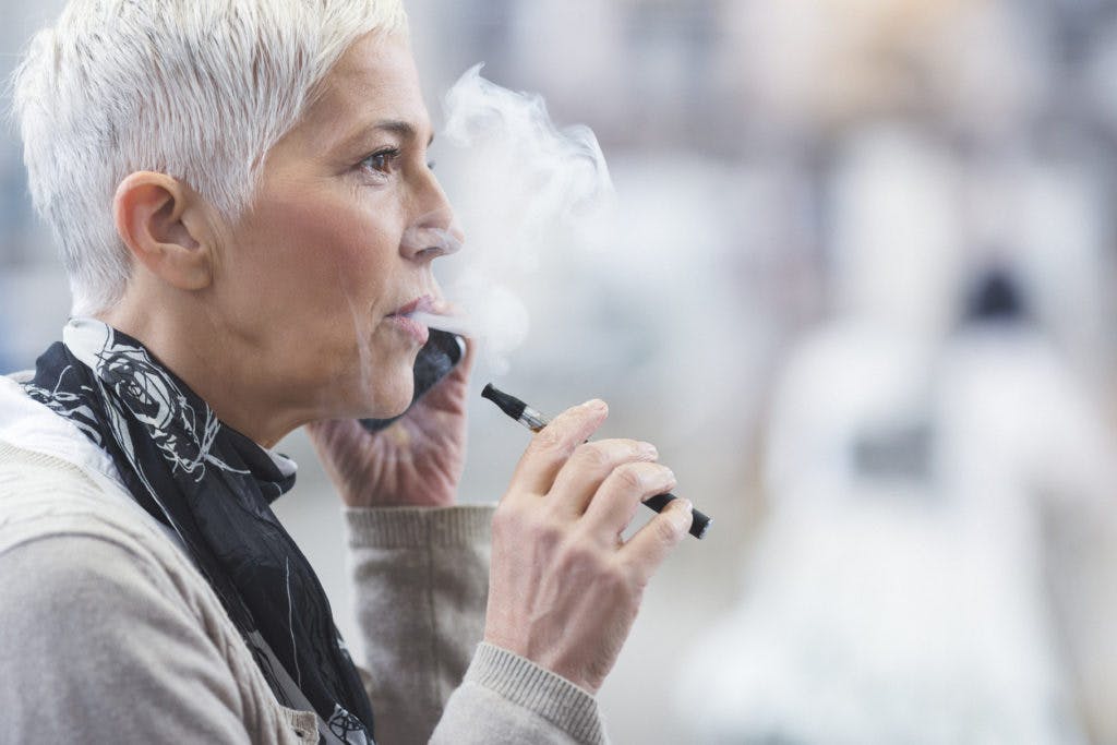 A senior woman enjoys an electronic cigarette-style vaporizer, by danchooalex via iStock