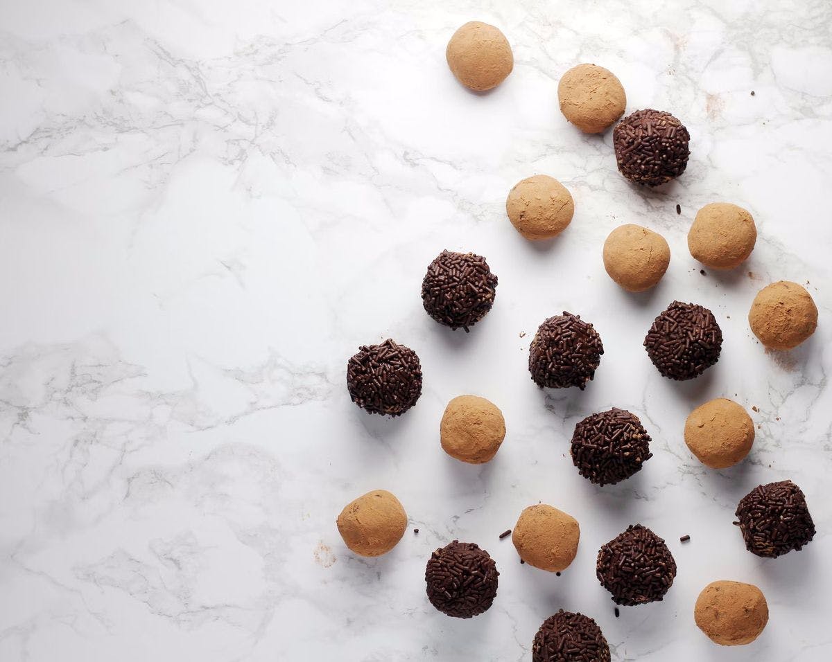 A selection of chocolate truffles on a white marble backdrop, by Sheri Silver via Unsplash