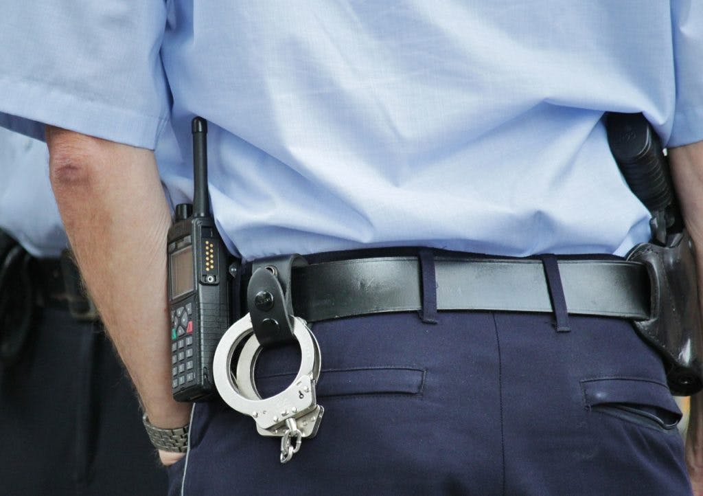 A police officer, wearing handcuffs and a radio, by cocoparisienne via Pixabay