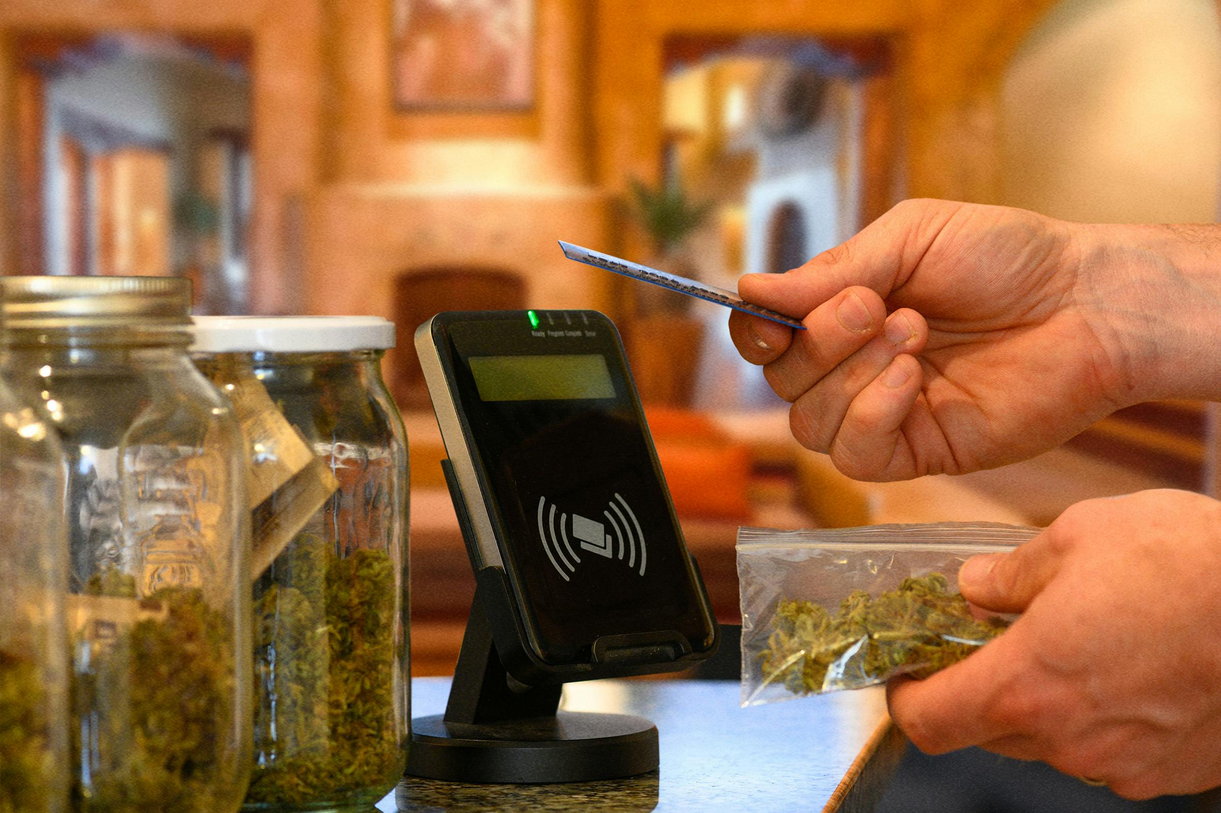 A hand is using a credit card to purchase cannabis at a dispensary