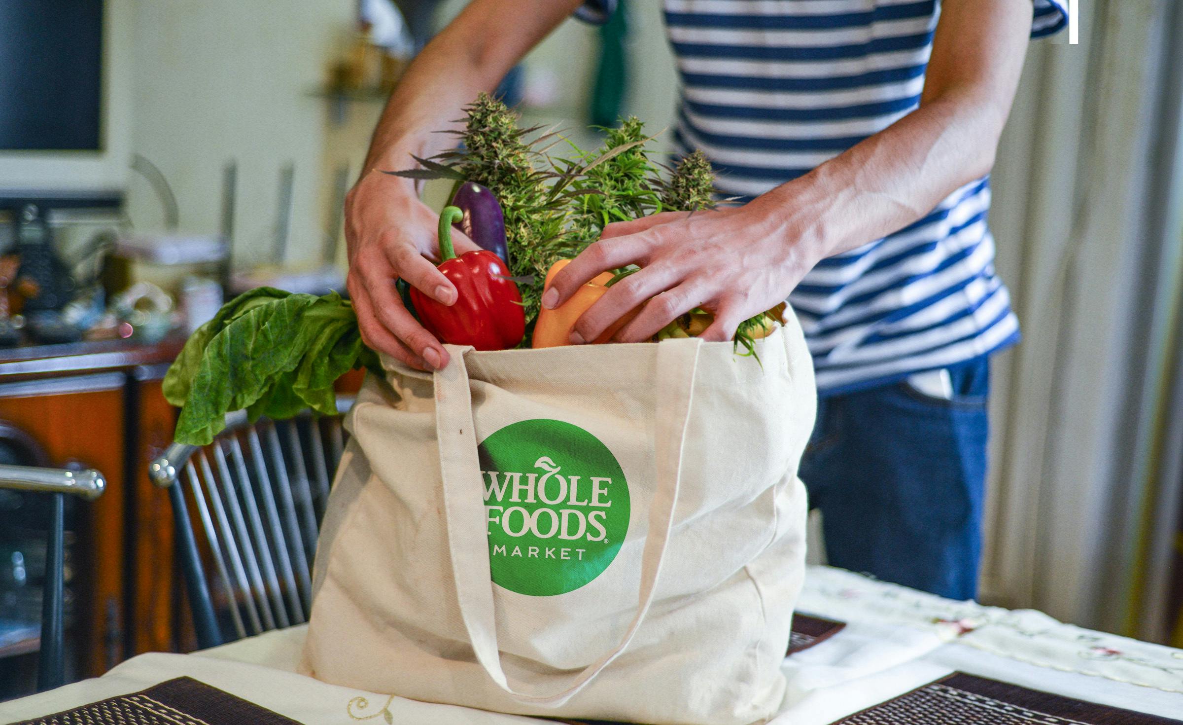 shopper packs Whole Foods grocery bag with produce and cannabis plants