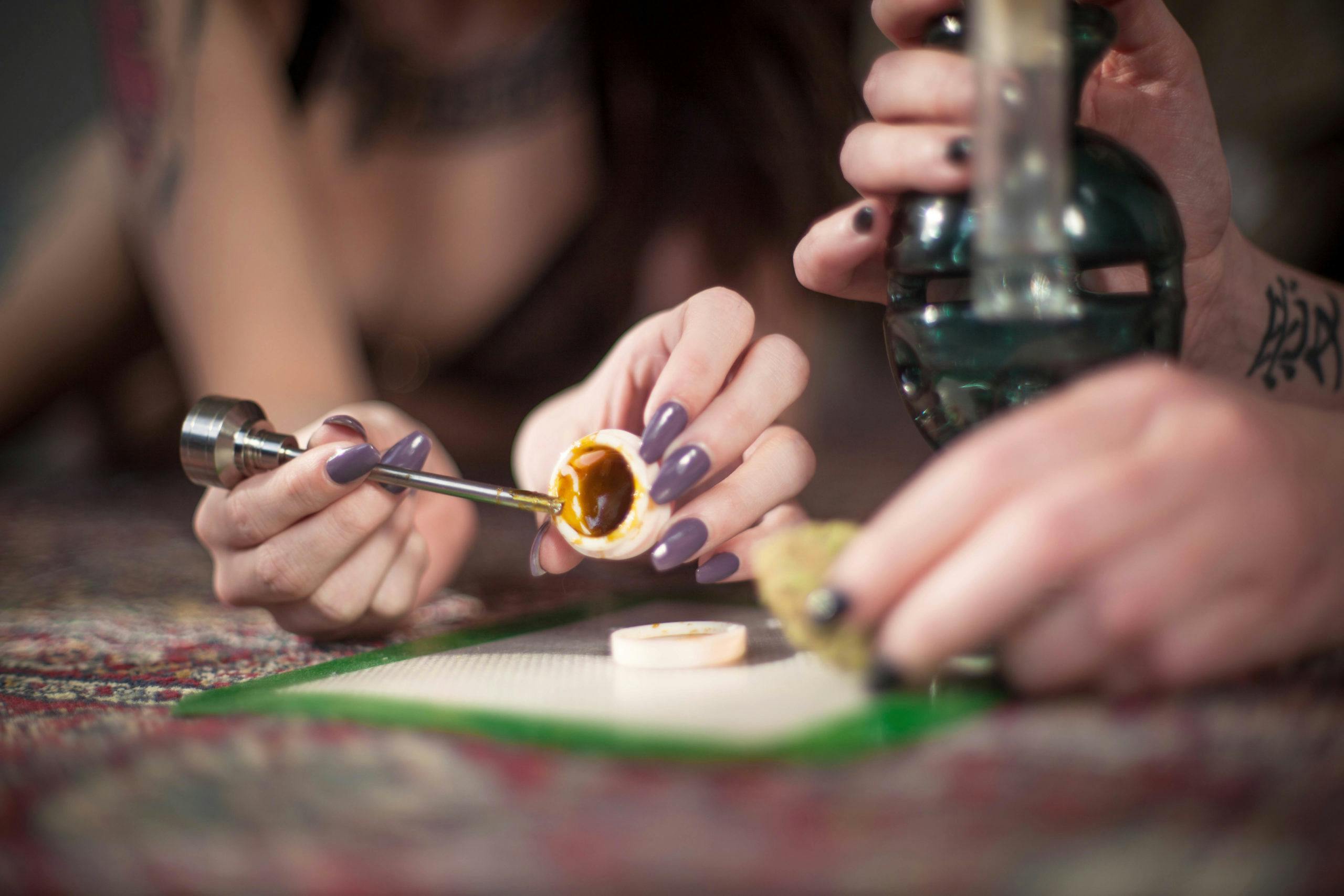 Two young ladies use a metal dabber to scoop concentrated THC ca
