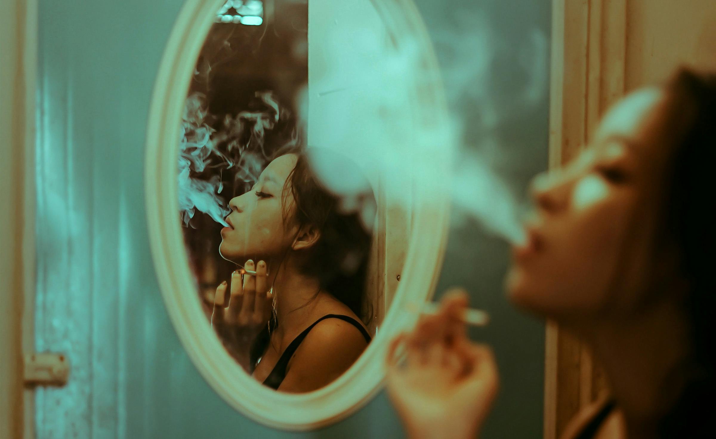 reflection in a mirror of a woman blowing out cannabis smoke