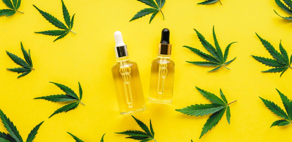 Hemp oil serum in glass dropper bottles with cannabis leaves. Cannabis leaf pattern with cosmetic product CBD oil on yellow background long web banner with copy space
