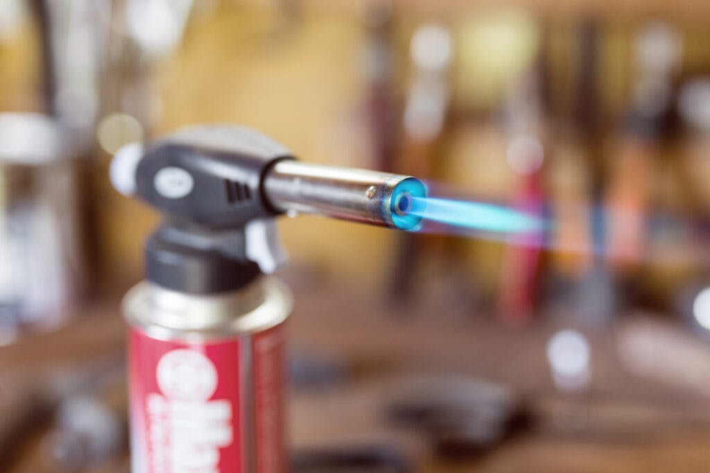 Gas cartridge gun lighter .Close-up nozzle of burner with blue flame jet. Workshop background, scorching of wood.