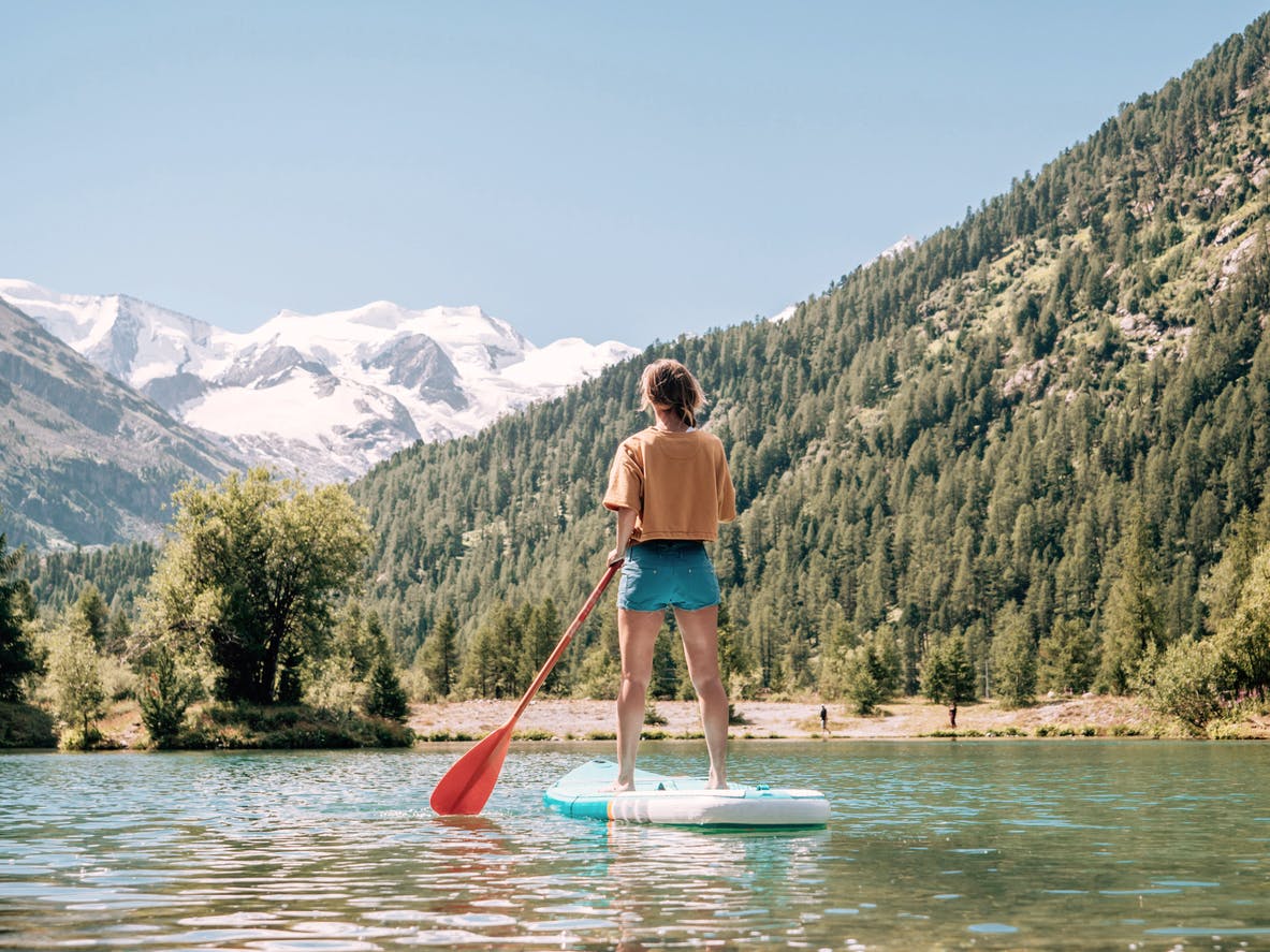 Stand up paddle with a view, woman on SUP in the mountains looking at glacier forest and mountain range. Girl enjoying outdoor activities on alpine lake