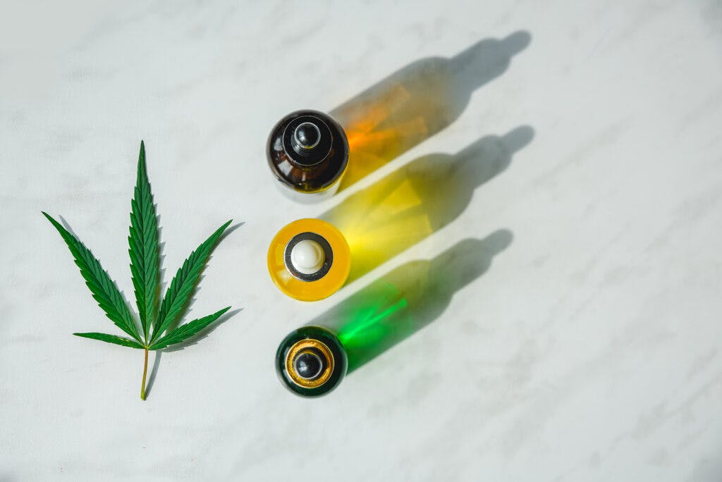 Glass bottle and dropper CBD OIL, THC tincture and cannabis leaf on background. Laboratory Production of cosmetics with CBD oil.