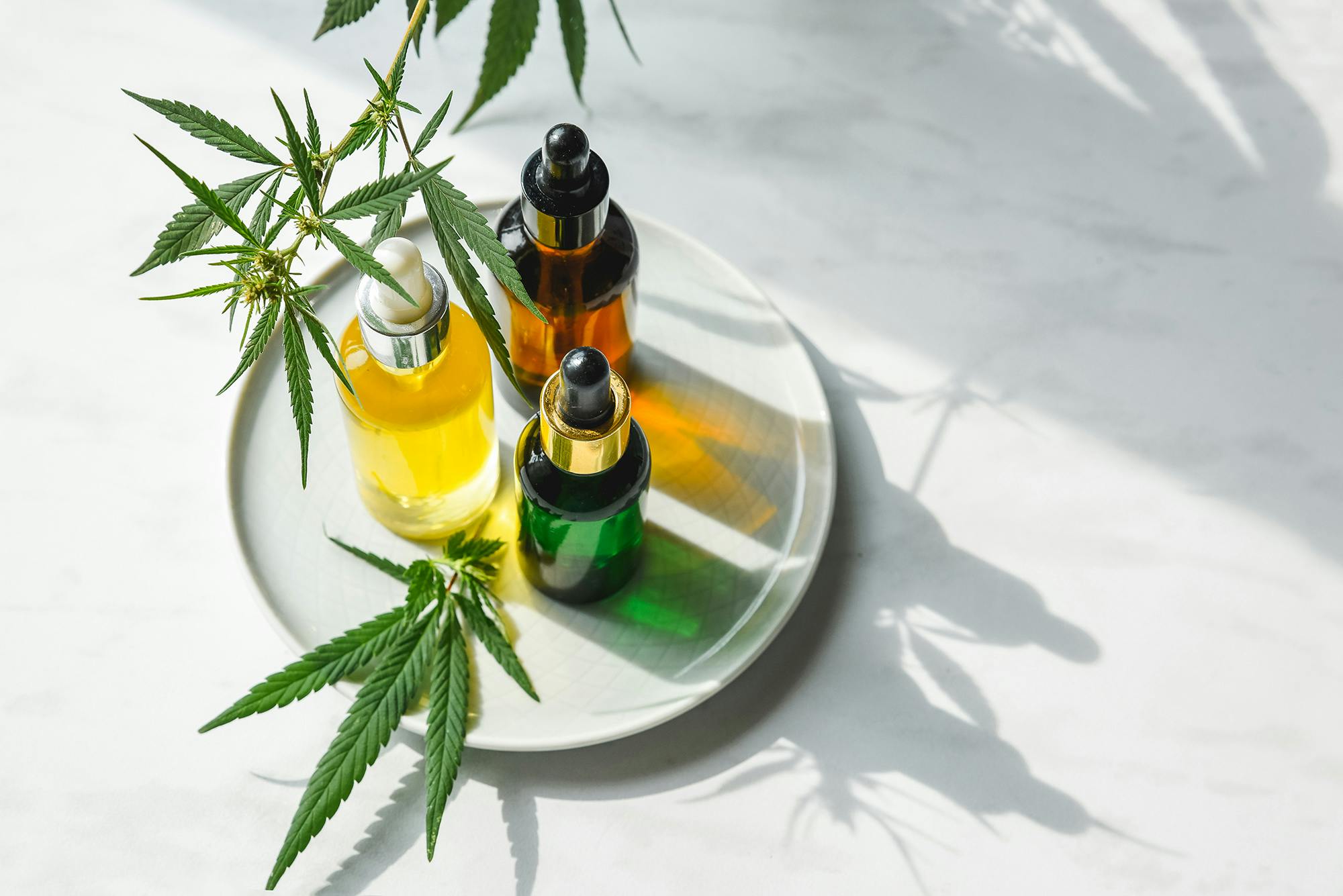 Different glass bottles with CBD OIL, THC tincture and cannabis leaves on yellow background. Flat lay, minimalism. Cosmetics CBD oil.