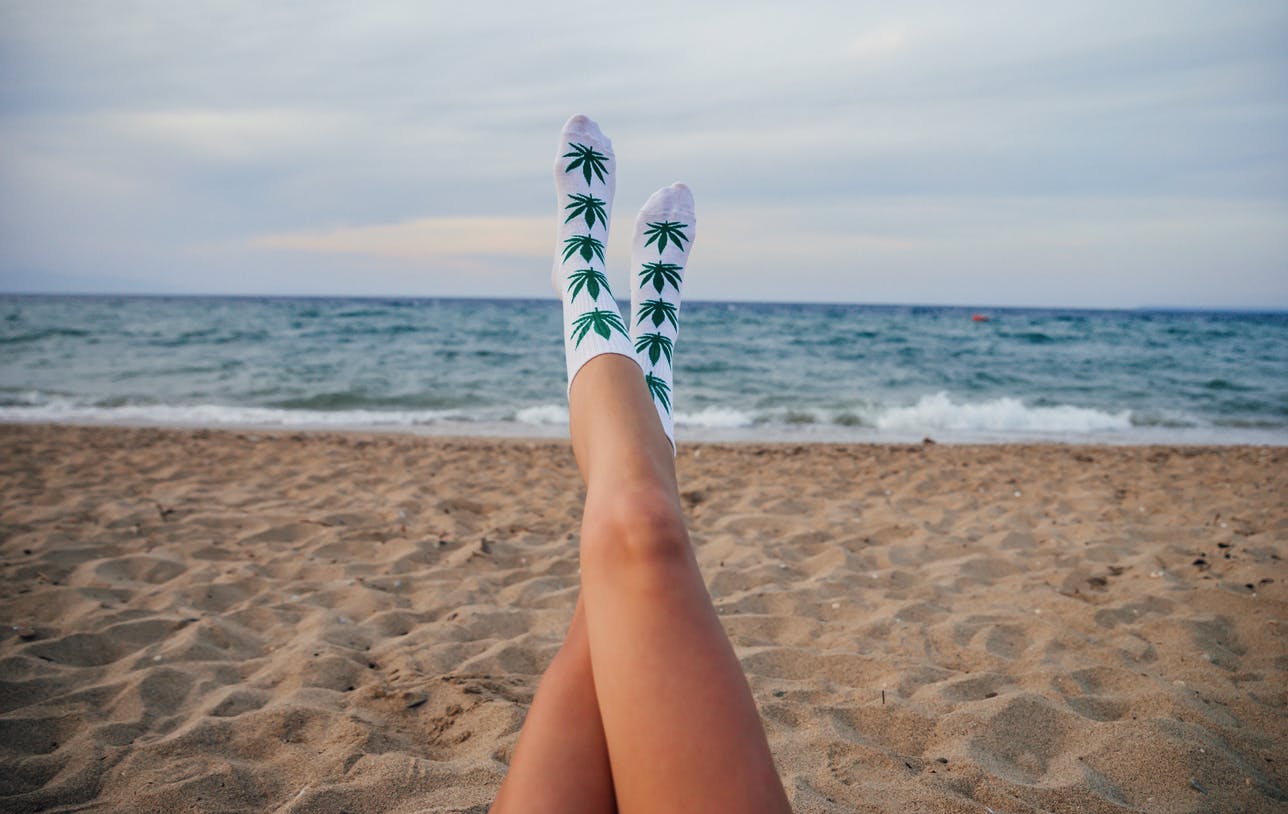 The legs of a woman wearing socks with images of cannabis leaf on the beach
