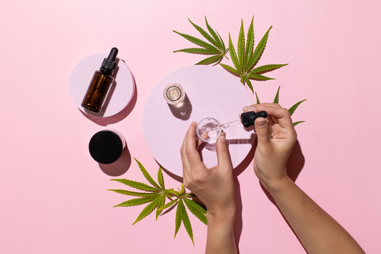 Bottles with CBD oil, THC tincture and cannabis leaves on pink background. Alternative cosmetics medical concept