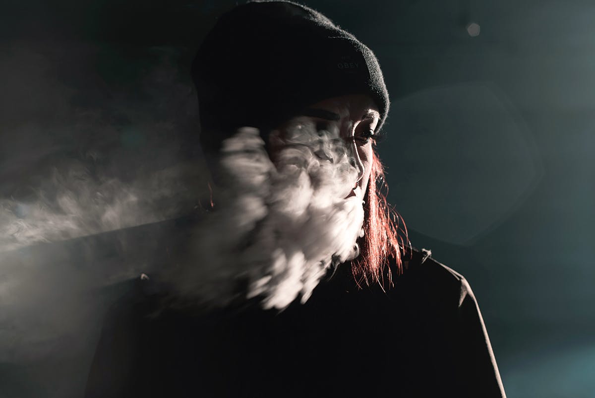 Portrait of woman with red hair blowing smoke in a dark room