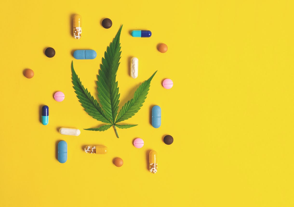 Cannabis leaf and many colorful pills on yellow background
