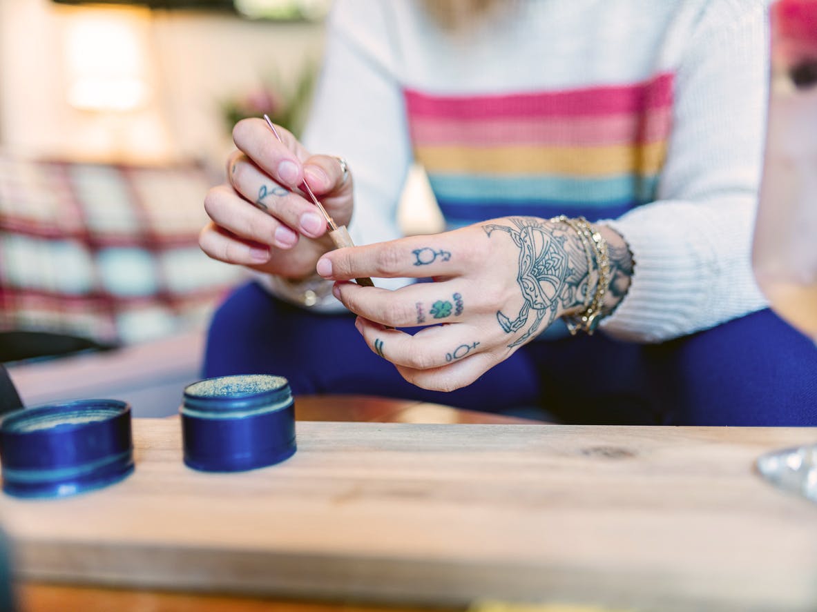 Close up of hands of Young woman with tattoos rolling up a joint of recreational marijuana. Interior of small apartment indoors.