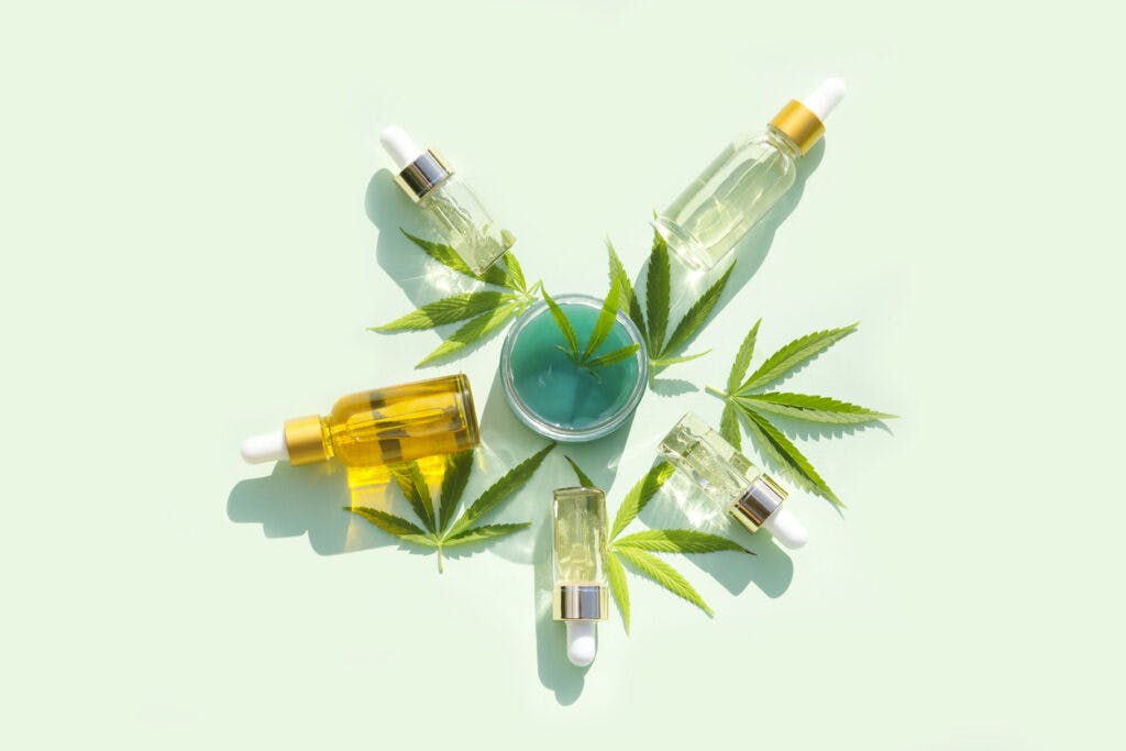 hemp cosmetic products glass bottles with oil,  seed extract and hemp  leaves on a mint background. Flat lay