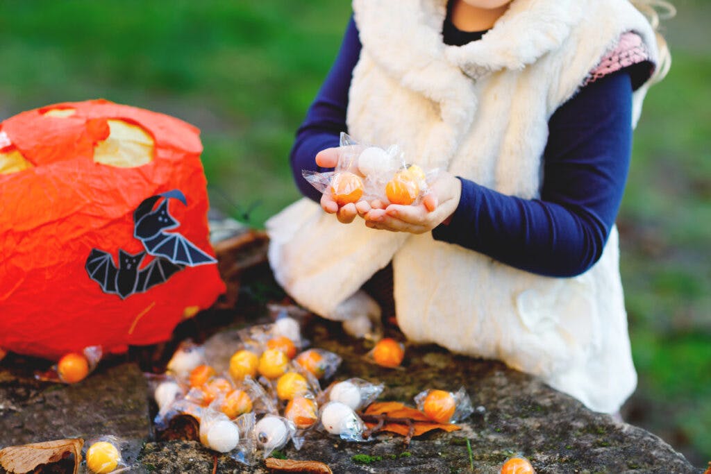 Closeup of toddler girl trick or treating on Halloween. Happy child outdoors counting sweets from pumpkin bag for sweet haunt. Family festival season in october. Outdoor activity. Trick or treat fun