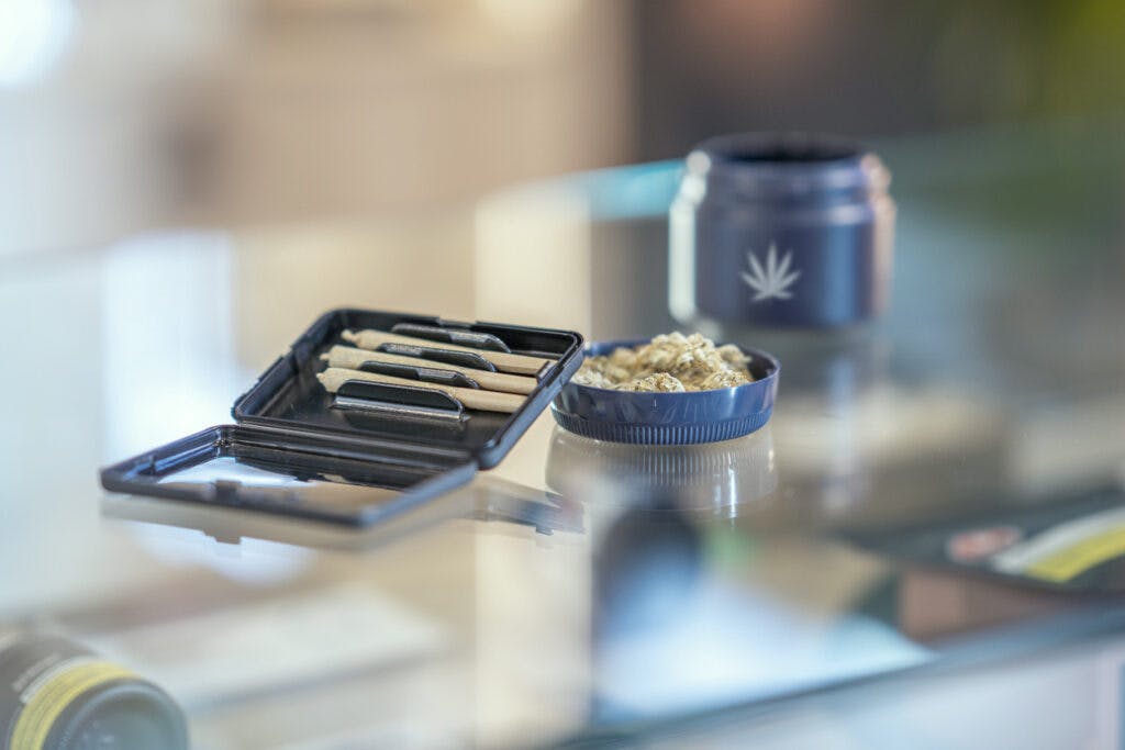 An assortment of cannabis product is laid out and displayed neatly on the counter of a legal retailer.  Joints and cannabis bulbs can be seen laying in their packaging on the glass counter.